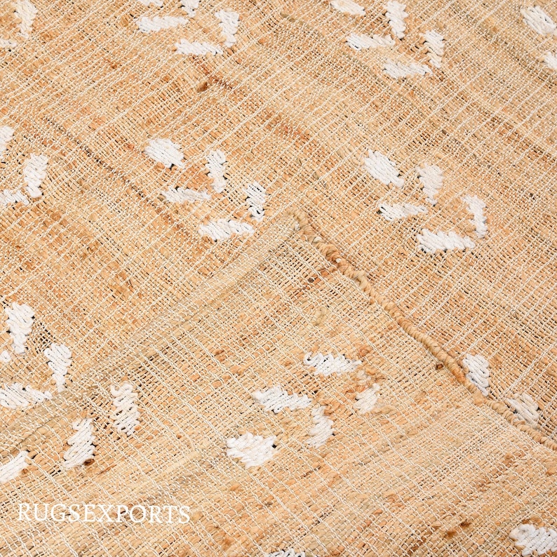 May include: A close-up of a beige woven rug with a white geometric pattern. The rug has a natural, rustic look and feel.