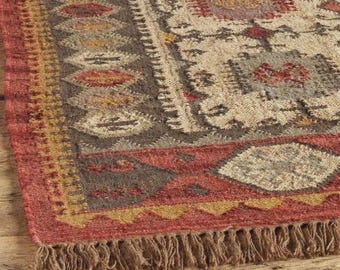 May include: A rectangular area rug featuring a woven texture with a geometric pattern in shades of red, brown, cream, and gold. The rug has a thick border with repeating diamond shapes and a fringe edge along the bottom short side.