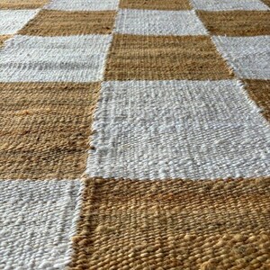 May include: A woven rug with a checkered pattern in brown and white. The rug is made of natural fibres and has a rustic look.