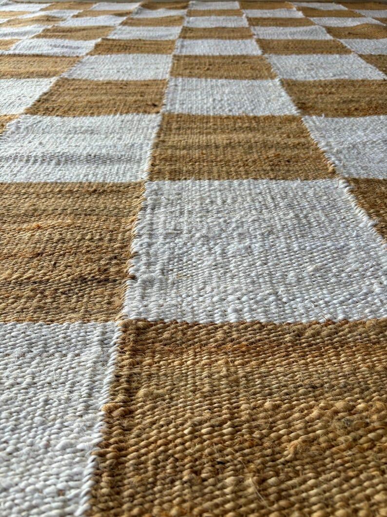 May include: A woven rug with a checkered pattern in brown and white. The rug is made of natural fibres and has a rustic look.