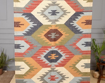 May include: A rectangular woven rug featuring a geometric pattern of interlocking hexagons in shades of rust orange, olive green, slate blue, and cream. The rug includes the text RUGSEXPORTS at the top and has fringed edges on the top and bottom.