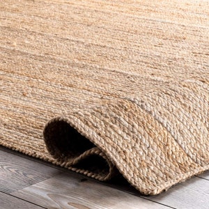 May include: Close-up of a natural fibre rug with a woven texture. The rug is a light brown colour and has a slightly frayed edge.