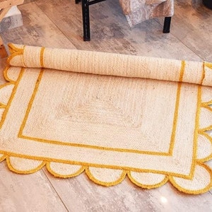 May include: A white and yellow jute rug with a scalloped edge and a square design in the center. The rug has a yellow border and a white center.