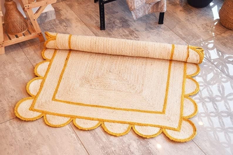 May include: A white and yellow jute rug with a scalloped edge and a square design in the center. The rug has a yellow border and a white center.