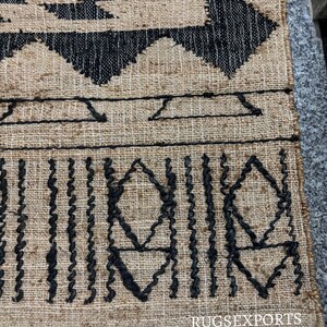 May include: A black and beige jute rug with a geometric pattern. The rug has a fringe border.