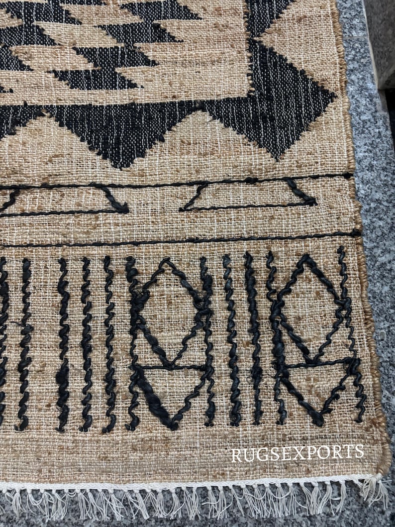 May include: A black and beige jute rug with a geometric pattern. The rug has a fringe border.
