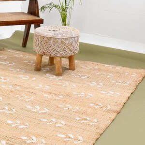 May include: A natural fiber rug with a white geometric pattern. A white woven stool with wooden legs sits on the rug.