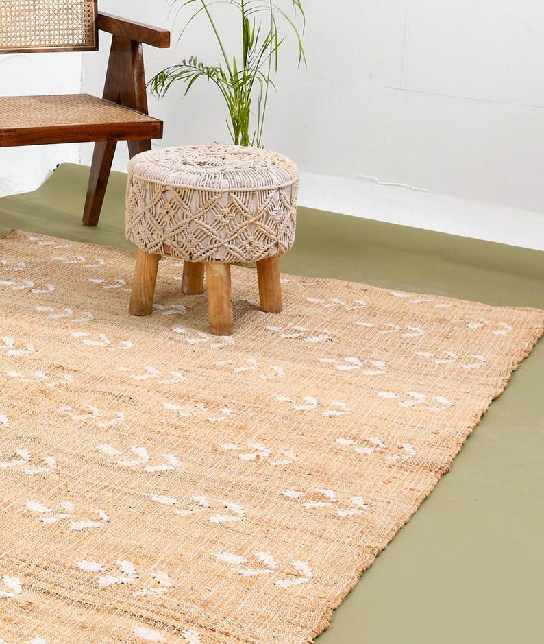 May include: A natural fiber rug with a white geometric pattern. A white woven stool with wooden legs sits on the rug.