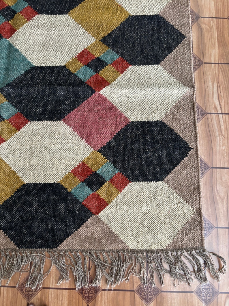 Pu&ograve; includere: Un tappeto geometrico con un motivo a rombi in vari colori. Il tappeto presenta una combinazione di nero, bianco, rosa, verde acqua, giallo senape e marrone. Il tappeto ha una frangia lungo il bordo inferiore.