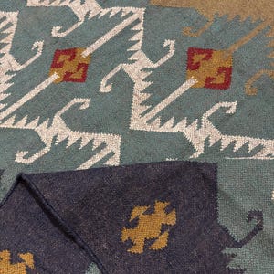 May include: A close-up of a blue and brown patterned rug with a geometric design. The rug has a fringe border and is made of a soft, woven material.
