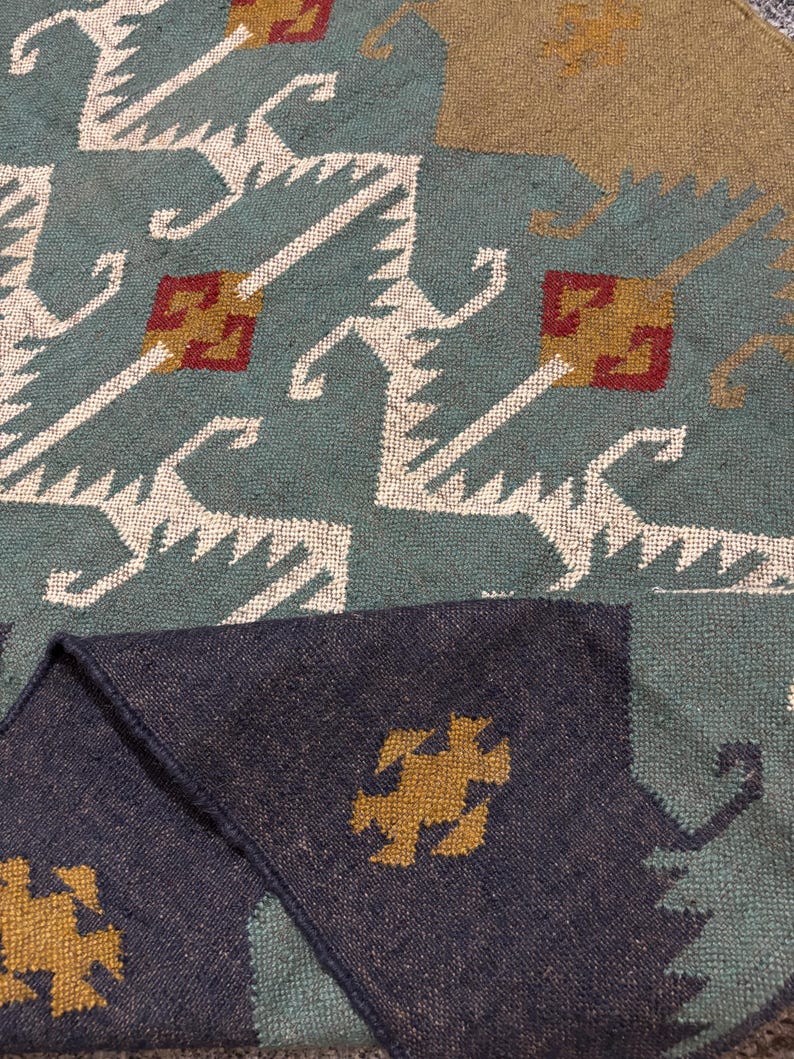 May include: A close-up of a blue and brown patterned rug with a geometric design. The rug has a fringe border and is made of a soft, woven material.