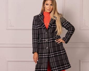 Puede incluir: Un abrigo largo de manga larga, a cuadros grises y negros, con cierre de un solo botón. El abrigo se lleva sobre un jersey rojo de cuello alto y unos pantalones anchos de color naranja.