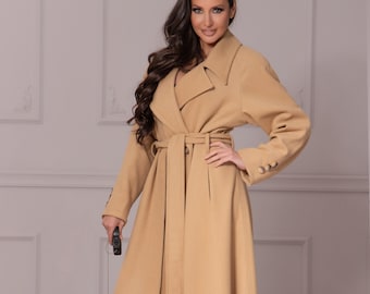 May include: A long, camel-colored coat with a matching belt and button details. The coat is worn with a matching outfit. A small dog in a matching coat is on a leash.
