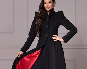 Könnte beinhalten: Ein langer schwarzer Mantel mit rotem Satin-Futter. Der Mantel hat einen hohen Kragen und einen Knopfverschluss. Das Model trägt den Mantel mit einem schwarzen Kleid und roten High Heels.