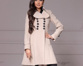 May include: A beige double-breasted coat with black buttons and a wide collar. The coat is worn over black pants and black heels.