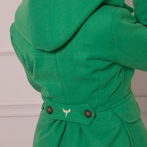 May include: A green hooded coat with a gold embroidered design on the back. The coat has two buttons on the back and a cinched waist.