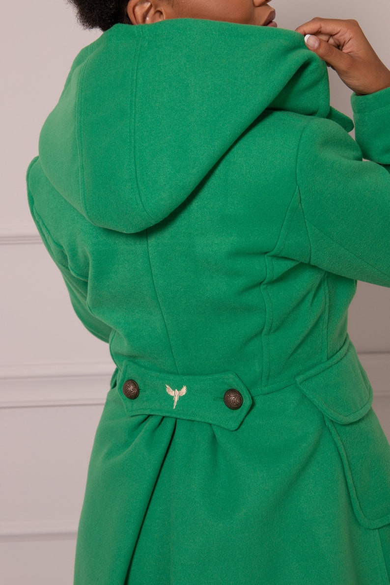 May include: A green hooded coat with a gold embroidered design on the back. The coat has two buttons on the back and a cinched waist.