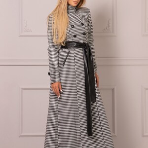May include: A long black and white checkered coat with a black leather belt and a long black leather tie. The coat has a double breasted closure and a high collar.