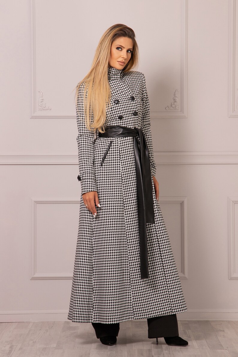 May include: A long black and white checkered coat with a black leather belt and a long black leather tie. The coat has a double breasted closure and a high collar.