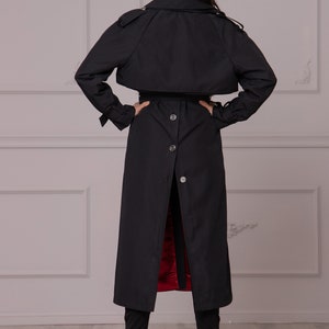 Puede incluir: Una gabardina negra con cintur&oacute;n y botones. La gabardina tiene un forro rojo y se muestra desde atr&aacute;s.