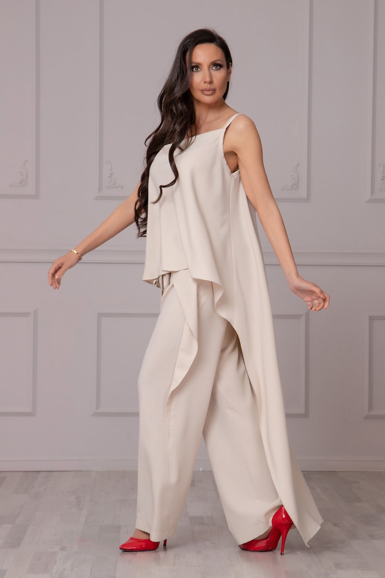 May include: A beige sleeveless top with a draped front and matching wide-leg pants. The outfit is made of a soft, flowing fabric and has a relaxed, comfortable fit.