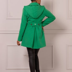 May include: A green hooded coat with a belt and buttons in the back. The coat is made of a soft, warm fabric and has a relaxed fit.