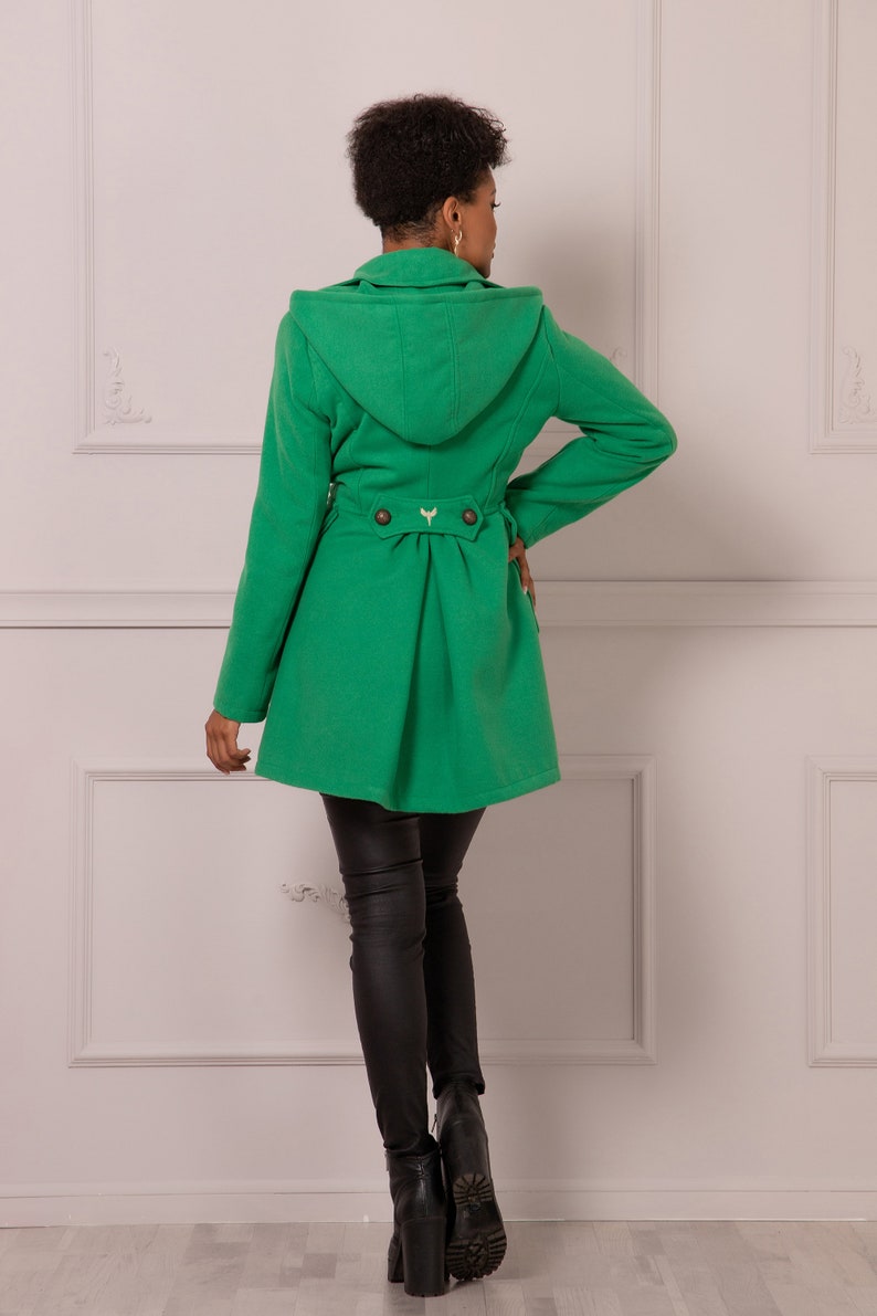 May include: A green hooded coat with a belt and buttons in the back. The coat is made of a soft, warm fabric and has a relaxed fit.
