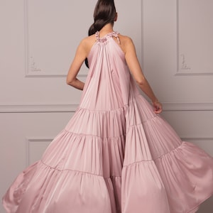 K&ouml;nnte beinhalten: Ein staubiges rosafarbenes Halstuchkleid mit einem flie&szlig;enden, mehrlagigen Rock. Das Kleid ist aus einem weichen, seidenartigen Stoff gefertigt und hat eine lockere Passform.