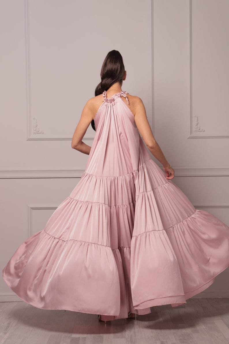 K&ouml;nnte beinhalten: Ein staubiges rosafarbenes Halstuchkleid mit einem flie&szlig;enden, mehrlagigen Rock. Das Kleid ist aus einem weichen, seidenartigen Stoff gefertigt und hat eine lockere Passform.