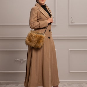K&ouml;nnte beinhalten: Eine Frau tr&auml;gt einen langen, camel-farbenen Mantel mit einer Tasche mit Pelzbesatz, die &uuml;ber ihrer Schulter h&auml;ngt. Sie tr&auml;gt rote High Heels.