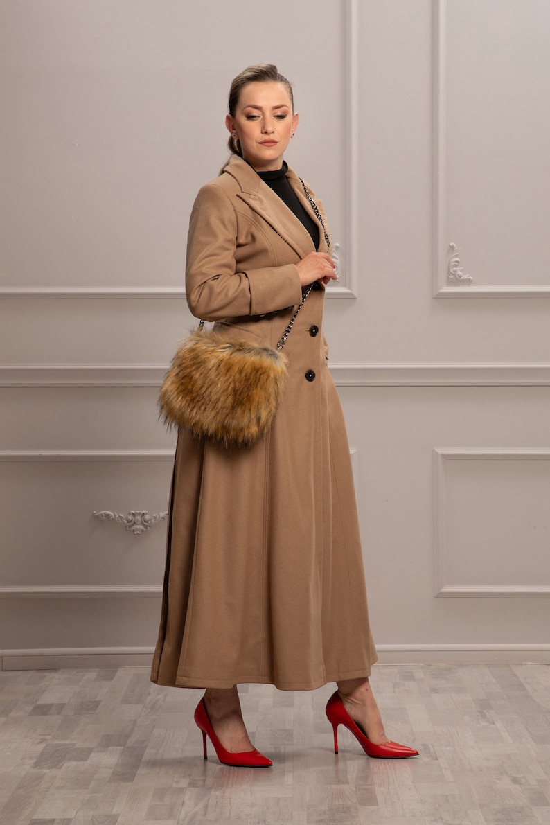K&ouml;nnte beinhalten: Eine Frau tr&auml;gt einen langen, camel-farbenen Mantel mit einer Tasche mit Pelzbesatz, die &uuml;ber ihrer Schulter h&auml;ngt. Sie tr&auml;gt rote High Heels.