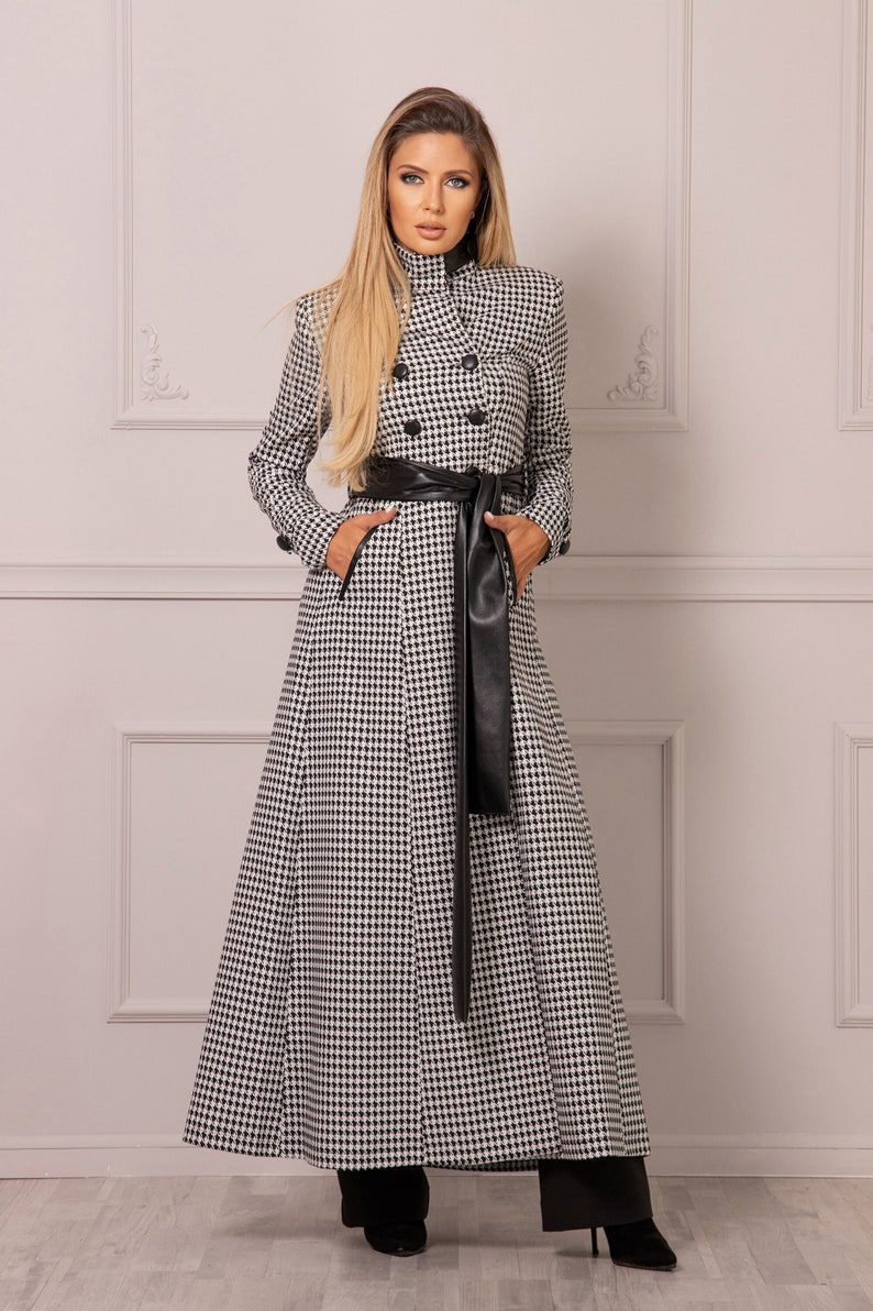 May include: A long black and white houndstooth coat with a black leather belt and a high collar.