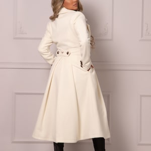 May include: A white long-sleeved coat with a flared skirt and a double-breasted closure. The coat has a high collar and two pockets.
