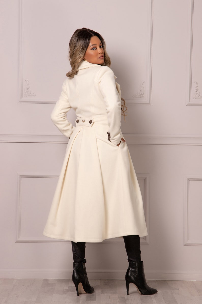 May include: A white long-sleeved coat with a flared skirt and a double-breasted closure. The coat has a high collar and two pockets.