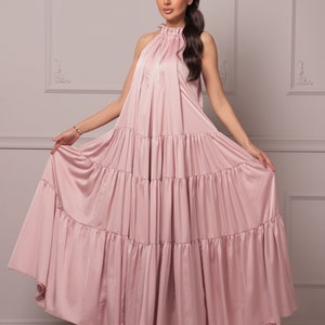 K&ouml;nnte beinhalten: Ein staubiges rosafarbenes Maxikleid mit einem Halterneck und mehreren Stufen. Das Kleid ist aus einem weichen, flie&szlig;enden Stoff gefertigt.