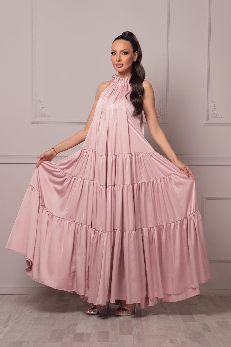 K&ouml;nnte beinhalten: Ein staubiges rosafarbenes Maxikleid mit einem Halterneck und mehreren Stufen. Das Kleid ist aus einem weichen, flie&szlig;enden Stoff gefertigt.