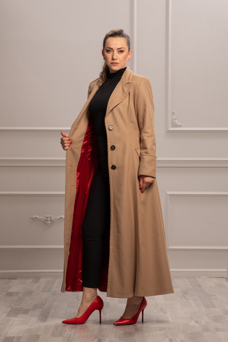 K&ouml;nnte beinhalten: Ein langer, beiger Mantel mit rotem Futter. Der Mantel hat einen Kragen, einen Knopfverschluss und lange &Auml;rmel. Das Model tr&auml;gt eine schwarze Hose und rote Schuhe mit Absatz.