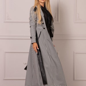 May include: A long black and white houndstooth coat with a black leather belt and a black collar. The coat has a double breasted closure and a long, flowing skirt.
