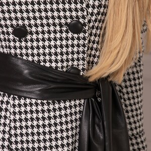 May include: A black and white houndstooth dress with a black leather belt. The belt is tied in a bow at the front of the dress.