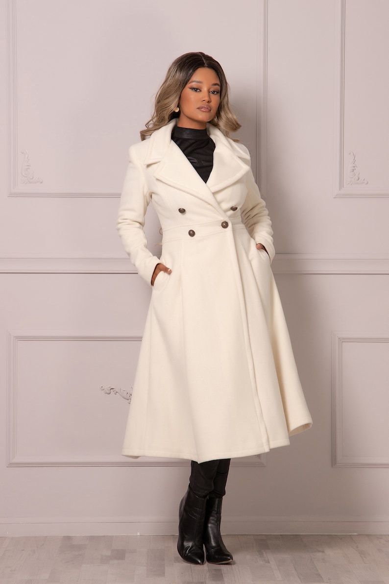 May include: A white double-breasted coat with a long, flowing skirt. The coat has a high collar and is belted at the waist.