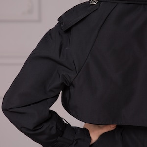 Puede incluir: Una gabardina negra con cierre de bot&oacute;n y cintur&oacute;n. La gabardina tiene un dise&ntilde;o cl&aacute;sico y est&aacute; hecha de una tela ligera.