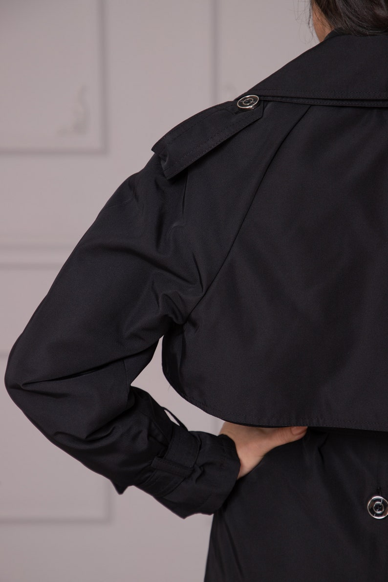 Puede incluir: Una gabardina negra con cierre de bot&oacute;n y cintur&oacute;n. La gabardina tiene un dise&ntilde;o cl&aacute;sico y est&aacute; hecha de una tela ligera.
