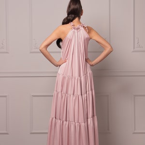 K&ouml;nnte beinhalten: Ein rosafarbenes, mehrlagiges Maxikleid mit einem Halterneck und einem gerafften Oberteil. Das Kleid ist aus einem weichen, flie&szlig;enden Stoff gefertigt und hat eine lockere Passform.