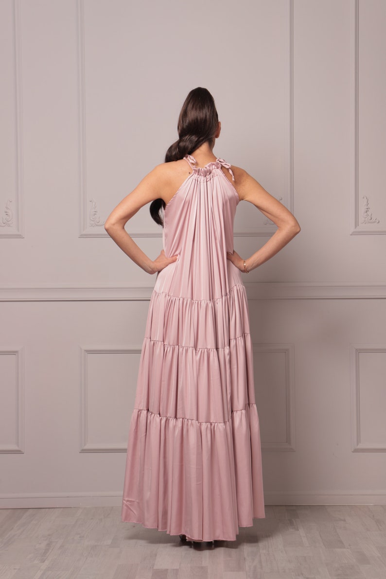 K&ouml;nnte beinhalten: Ein rosafarbenes, mehrlagiges Maxikleid mit einem Halterneck und einem gerafften Oberteil. Das Kleid ist aus einem weichen, flie&szlig;enden Stoff gefertigt und hat eine lockere Passform.