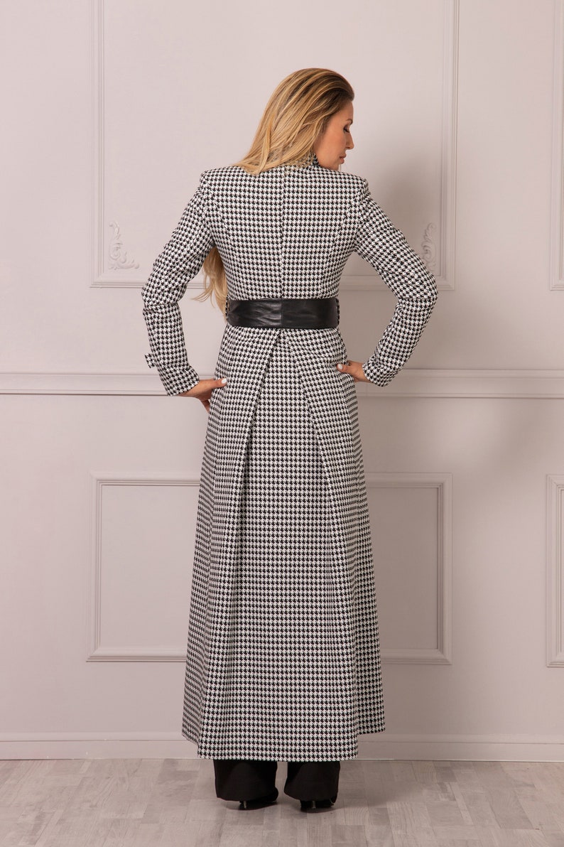 May include: A long black and white houndstooth coat with a black leather belt. The coat has a long skirt and is fitted at the waist.