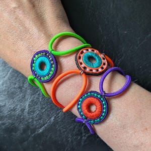 Pulseras coloridas y alegres con medallones de cuentas, rosetas de ganchillo envueltas en hilo de coser y cosidas con cinta de soutache. Pura alegría veraniega de Le Tact.
