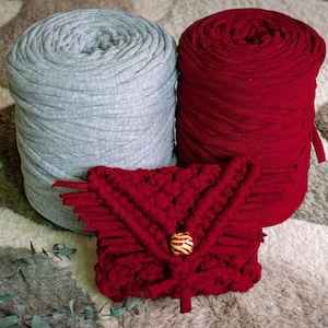 May include: Two spools of yarn, one gray and one red, with a red crocheted pouch with a wooden button in the center.