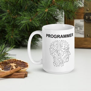 Op de afbeelding: Witte keramische mok met een zwart printje van een printplaat in de vorm van een hoofd en het woord "PROGRAMMEUR" in het zwart bovenaan.