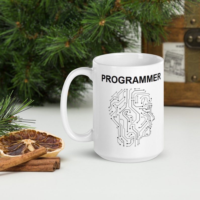 Op de afbeelding: Witte keramische mok met een zwart printje van een printplaat in de vorm van een hoofd en het woord "PROGRAMMEUR" in het zwart bovenaan.