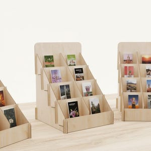 Puede incluir: Un expositor escalonado de madera clara con múltiples ranuras inclinadas diseñadas para sostener y mostrar tarjetas o folletos rectangulares. La estructura está compuesta por paneles de madera contrachapada entrelazados con un acabado natural.